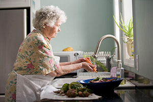 elderly woman preparing food at sink experiencing reduced pain from arthritis due to hypnotherapy